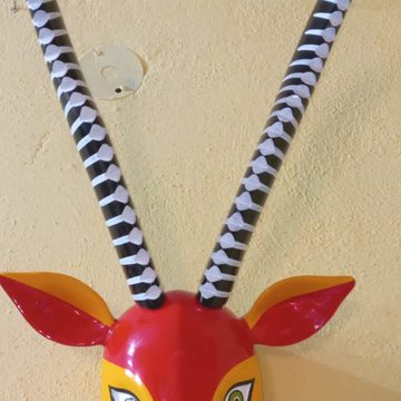 Acercamiento a la máscara de chivo: base de los cuernos negros con anillos blancos en relieve, orejas rojas y frente amarilla