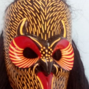 Acercamiento a la máscara del nahual café: trazos amarillos sobre café oscuro y ojos rodeados de discos rojos