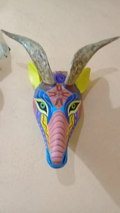 Máscara de chivo con cuernos jaspeados, orejas amarillas y rostro azul, morado y rosa con líneas onduladas