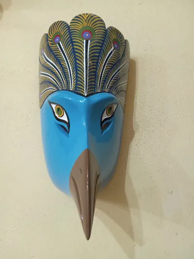 Máscara de ave de rostro azul celeste, pico largo café y penacho con plumas de pavo real