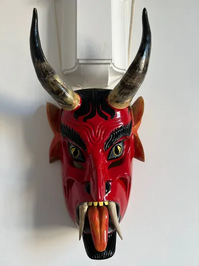 Máscara de diablo rojo brillante con cuernos largos, cejas negras talladas, colmillos y lengua anaranjada