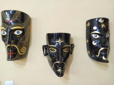 Tres máscaras de rostro humano en negro brillante con estrellas, lunas, puntos y bigotes dorados