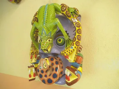 Máscara de rostro lila cubierta por una iguana verde, serpientes amarillas manchadas y un animal enroscado de manchas azules