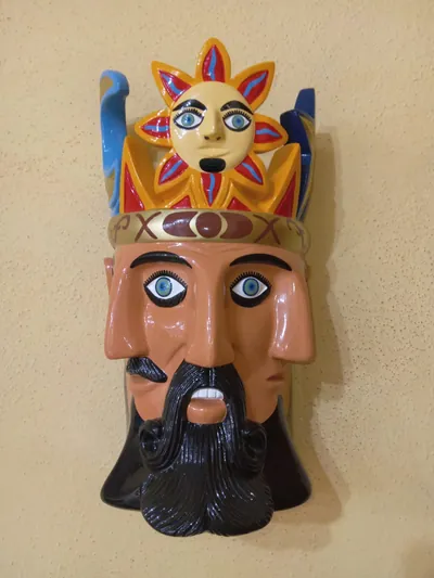 Máscara de El Tiempo de frente: tres rostros con barba negra rizada, diadema dorada y un sol con cara en la corona