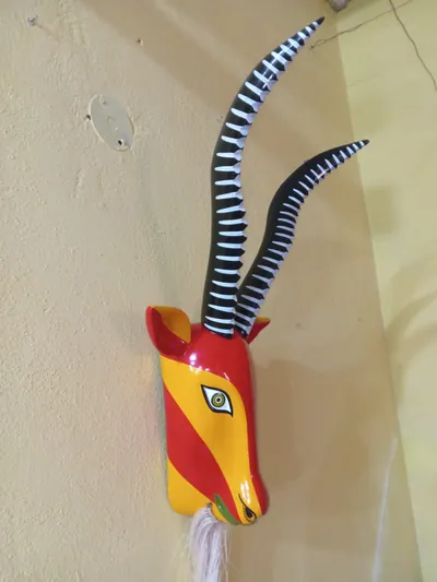 Máscara de chivo con franjas rojas y amarillas, cuernos largos negros con anillos blancos y barba de fibra blanca