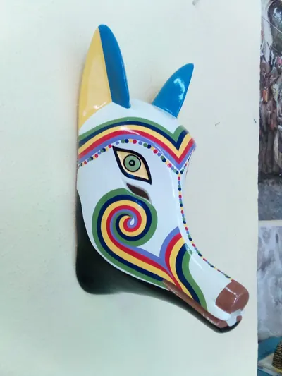 Máscara de coyote blanca con franjas de arcoíris, espiral en la mejilla, orejas amarillas y azules y nariz café