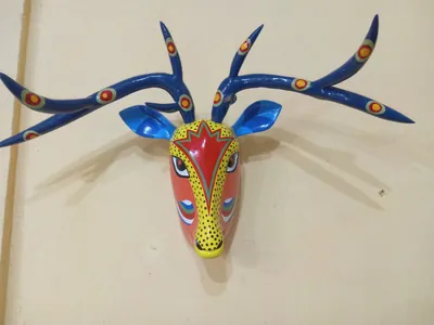Máscara de venado con cara anaranjada y amarilla y grandes astas azules ramificadas con círculos de colores