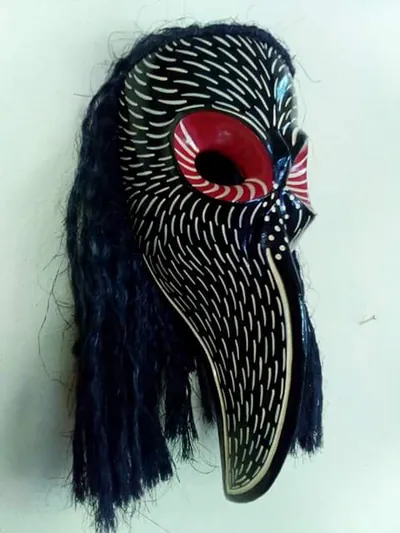 Máscara negra de pico largo con trazos crema, ojo rojo y cabellera de fibra oscura, vista de perfil