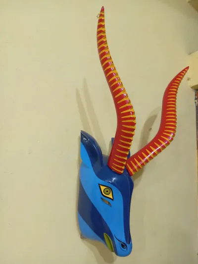 Máscara de chivo azul con largos cuernos rojos y amarillos, colgada de perfil en una pared crema