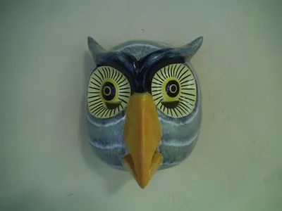 Máscara de búho gris azulado con ojos amarillos de rayos negros y pico amarillo, de frente sobre pared blanca