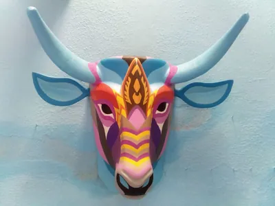 Máscara de toro con cuernos azul claro y cara de franjas rosas, moradas y amarillas sobre pared azul