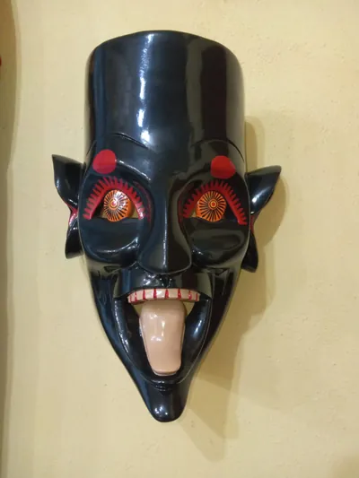 Máscara negra brillante con ojos anaranjados en forma de sol, orejas puntiagudas y la lengua de fuera
