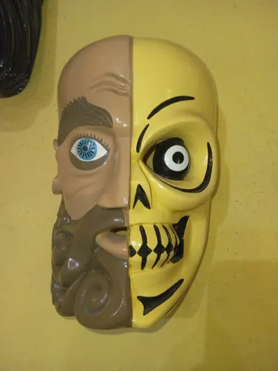 Máscara de rostro partido: mitad hombre barbado de ojo azul y mitad calavera amarilla