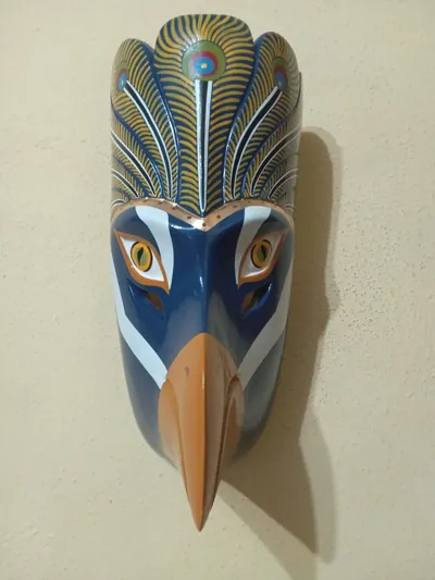 Máscara de ave azul con pico anaranjado y copete de plumas amarillas y azules con ojos de pavo real
