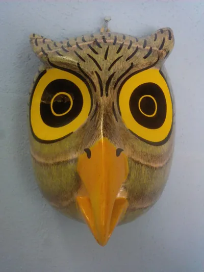 Máscara de búho gris verdoso con grandes ojos amarillos y negros y pico amarillo sobre pared azul