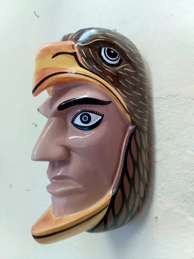 Máscara de rostro humano de perfil dentro de una cabeza de águila café con pico amarillo