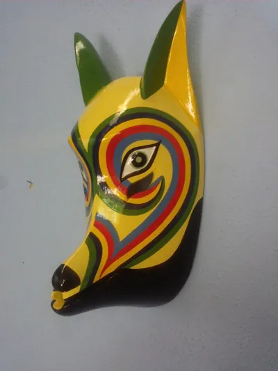 Máscara amarilla de coyote con orejas verdes y franjas de arcoíris alrededor del ojo, de perfil