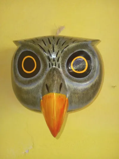 Máscara de búho gris con ojos negros de anillo anaranjado y pico anaranjado sobre pared amarilla