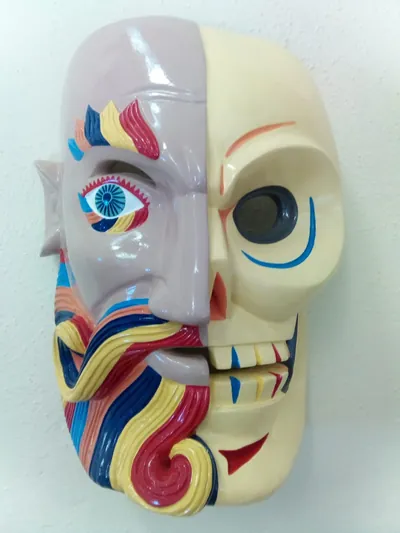 Máscara partida: mitad rostro humano malva con barba de colores y mitad calavera color crema