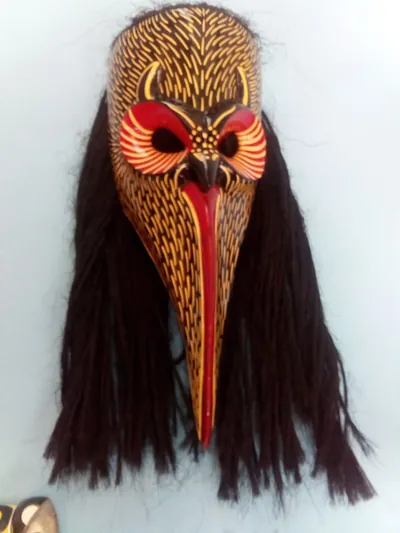 Máscara de nahual café con plumas amarillas pintadas, ojos rojos y larga cabellera de fibra oscura