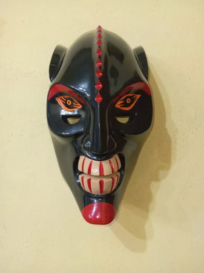 Máscara negra con cresta de picos rojos en la frente, ojos anaranjados y sonrisa de dientes rayados