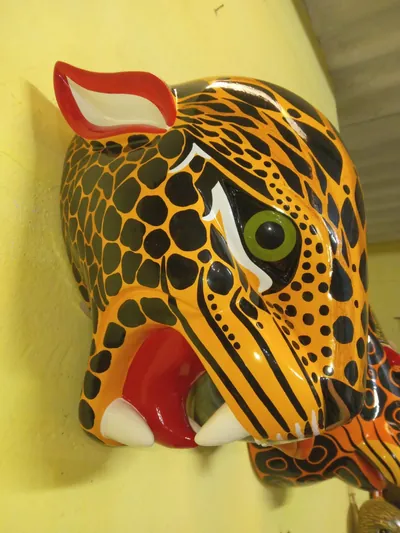 Cabeza de jaguar anaranjada con manchas negras, ojo verde y fauces abiertas con colmillos blancos
