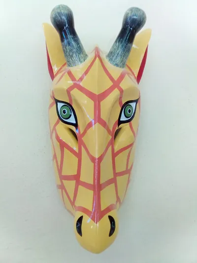 Máscara de jirafa amarilla con líneas color coral, cuernitos grises y ojos verdes, de frente