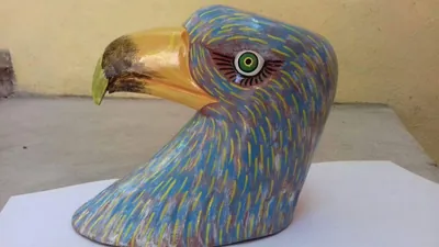 Máscara de águila azul con trazos amarillos, ojo verde con pestañas y pico curvo amarillo