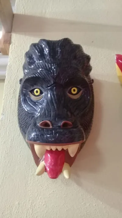 Máscara de gorila negra con pelo tallado, ojos amarillos, colmillos color hueso y lengua roja de fuera