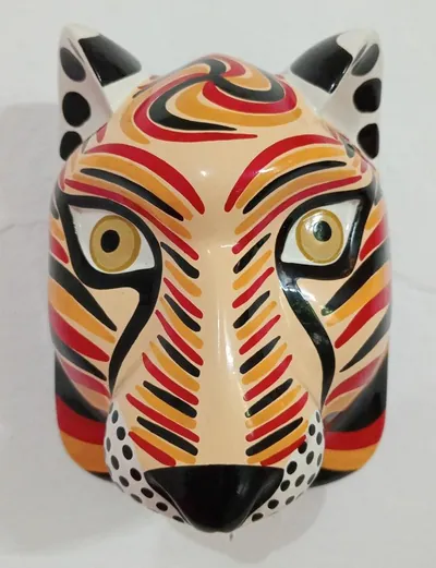 Máscara de lince crema con rayas rojas, anaranjadas y negras, orejas con manchas y hocico punteado, de frente en pared blanca